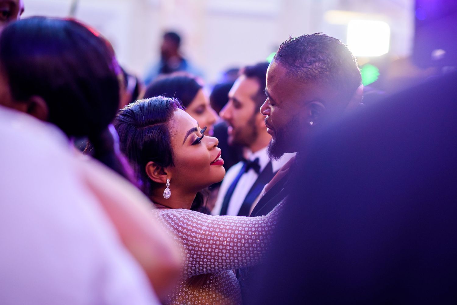Wedding reception dance floor filled with guests under purple mood lighting.