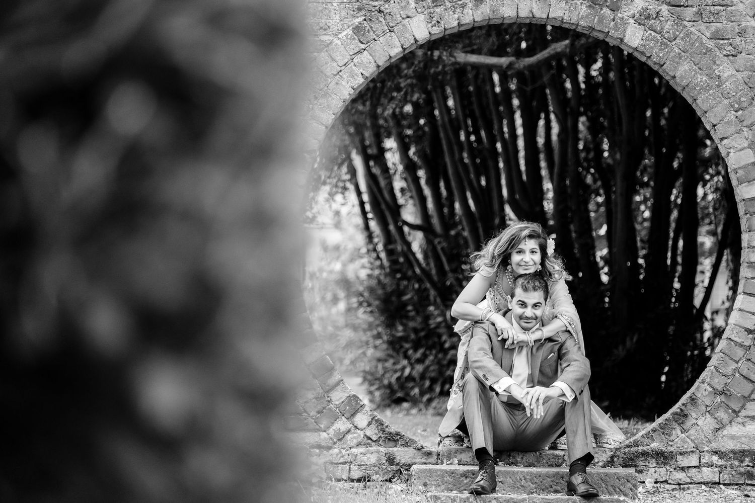 Dramatic black and white engagement photos captured through a stone archway.