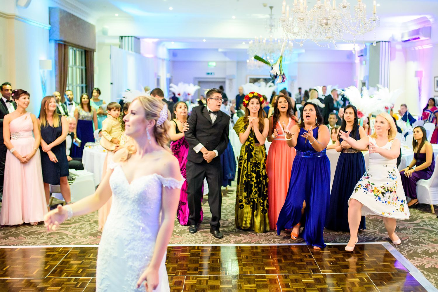 Large group of wedding guests dancing and celebrating in a luxuriously decorated ballroom.