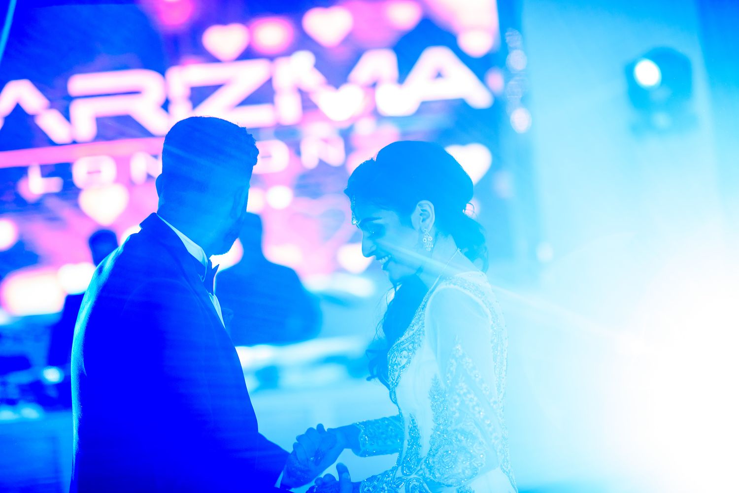 Colorful blue and pink lighting illuminates a lively crowd at an indoor celebration.