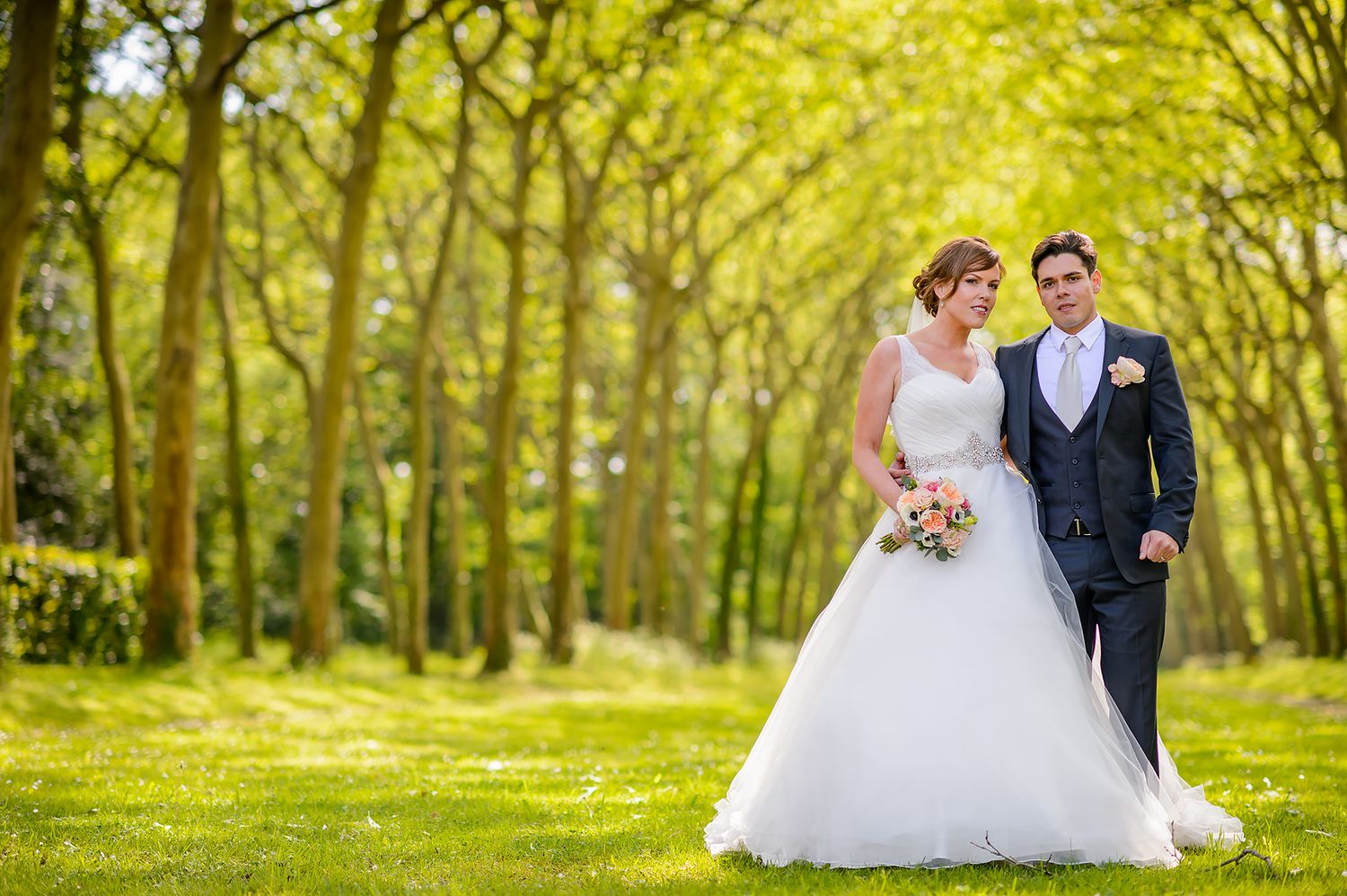 Newlyweds walking through lush green springtime forest setting.