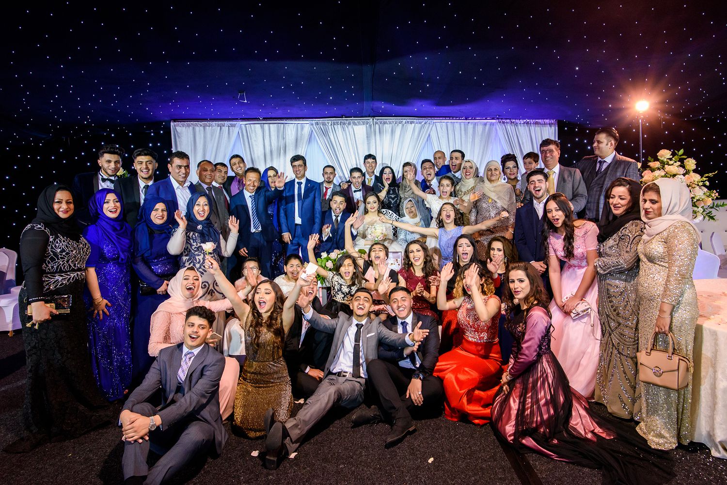 Large group photo of wedding guests gathered outside at night for a celebration.