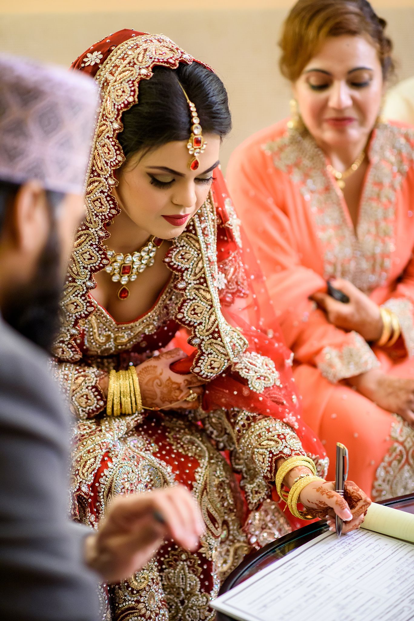 Bride in traditional Indian wedding attire signing documents during ceremony.