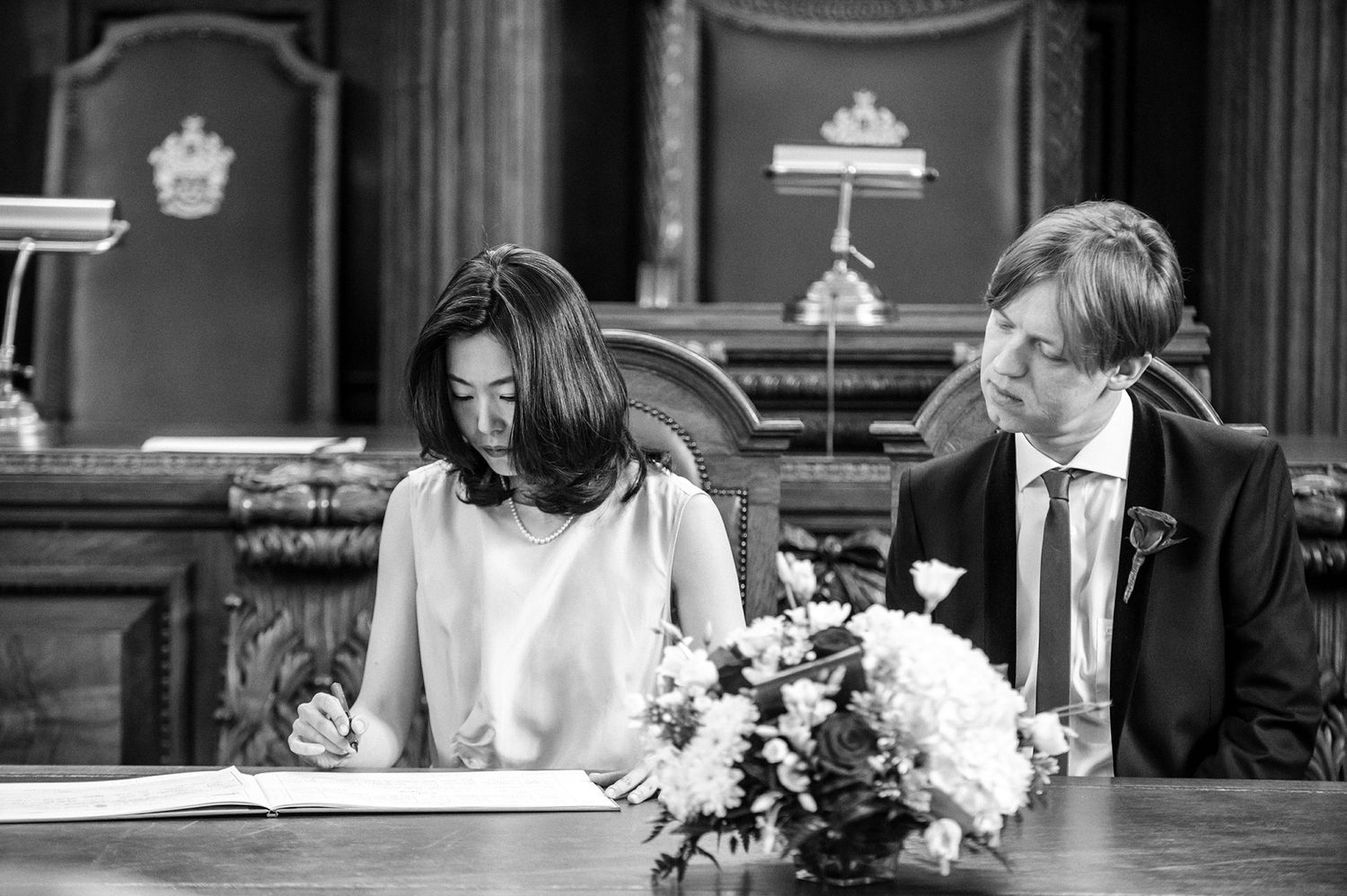 Wedding ceremony in a historic venue with wooden paneling and floral arrangements.