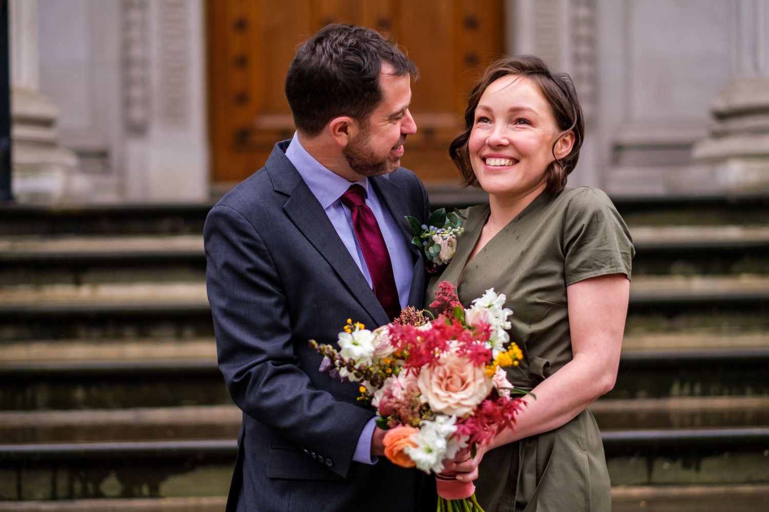 Couple sharing a joyful moment on stone steps while holding a vibrant floral bouquet.