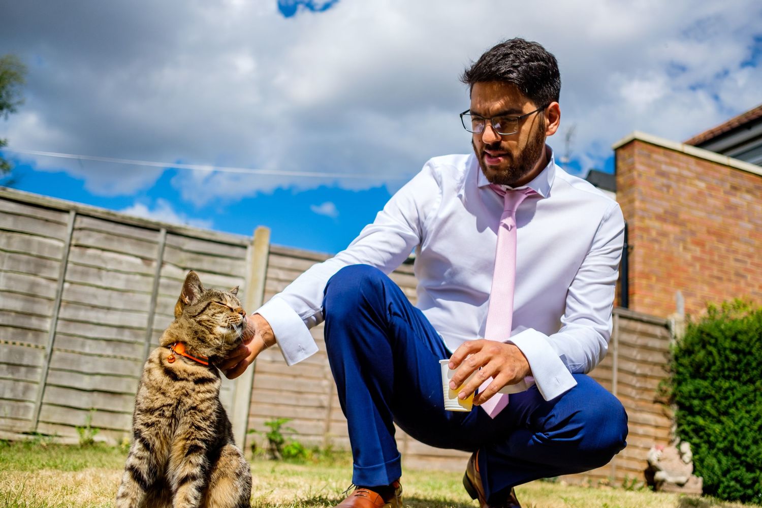 A cat watches curiously as someone in blue pants and white shirt sits in an outdoor garden.