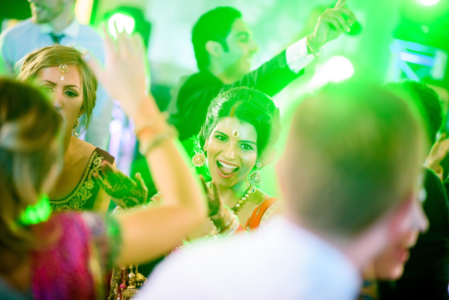 Dreamy green lighting effects capture the joyful atmosphere of wedding guests dancing.
