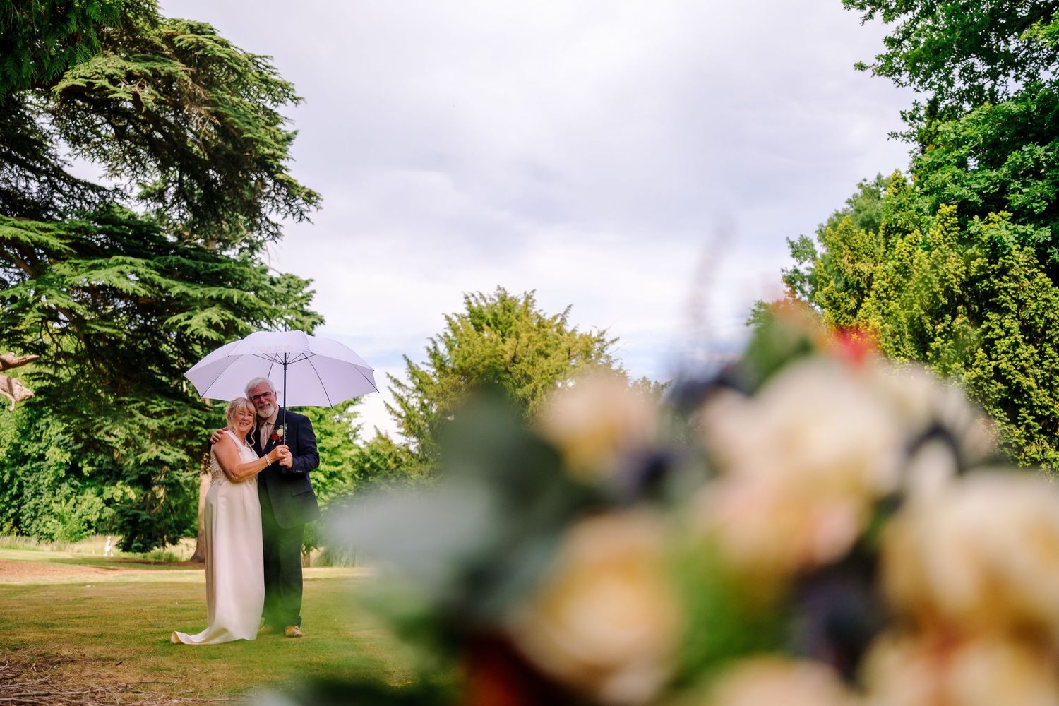 Wedding couple photographed from a distance in a lush green outdoor setting.