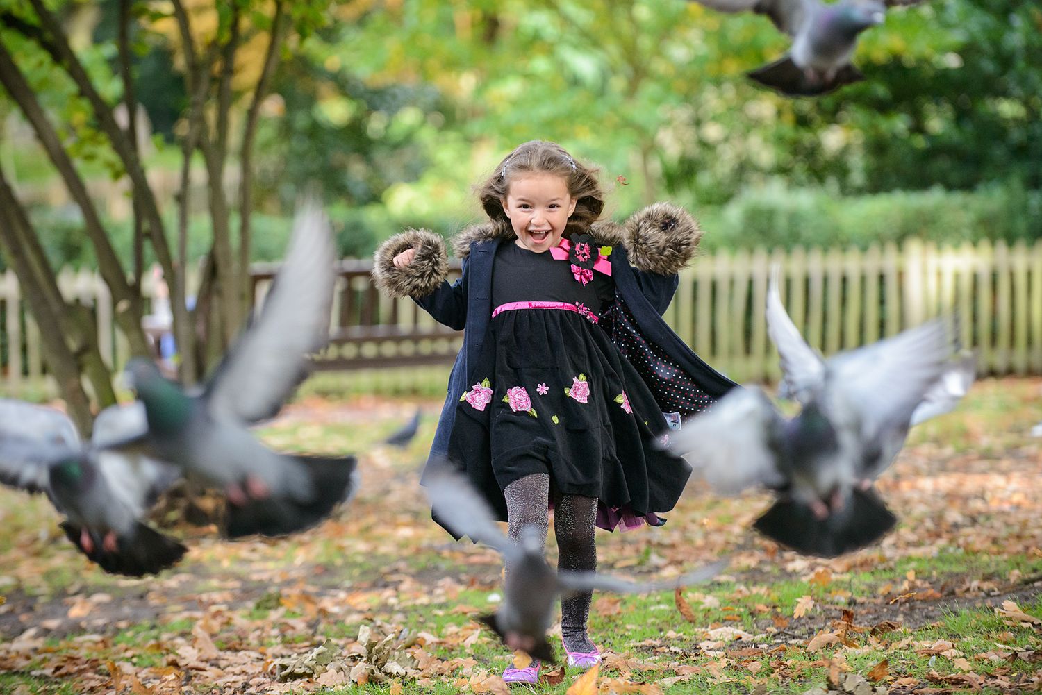 Children chasing pigeons in a lush garden setting on a sunny day.