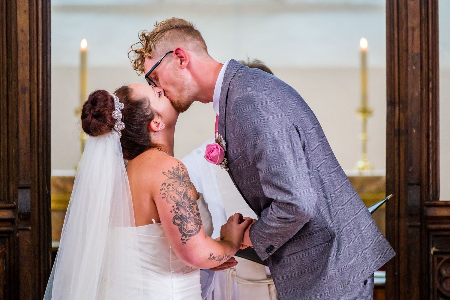 Romantic wedding ceremony kiss between couple in a church with wooden paneled walls and stained glass windows.