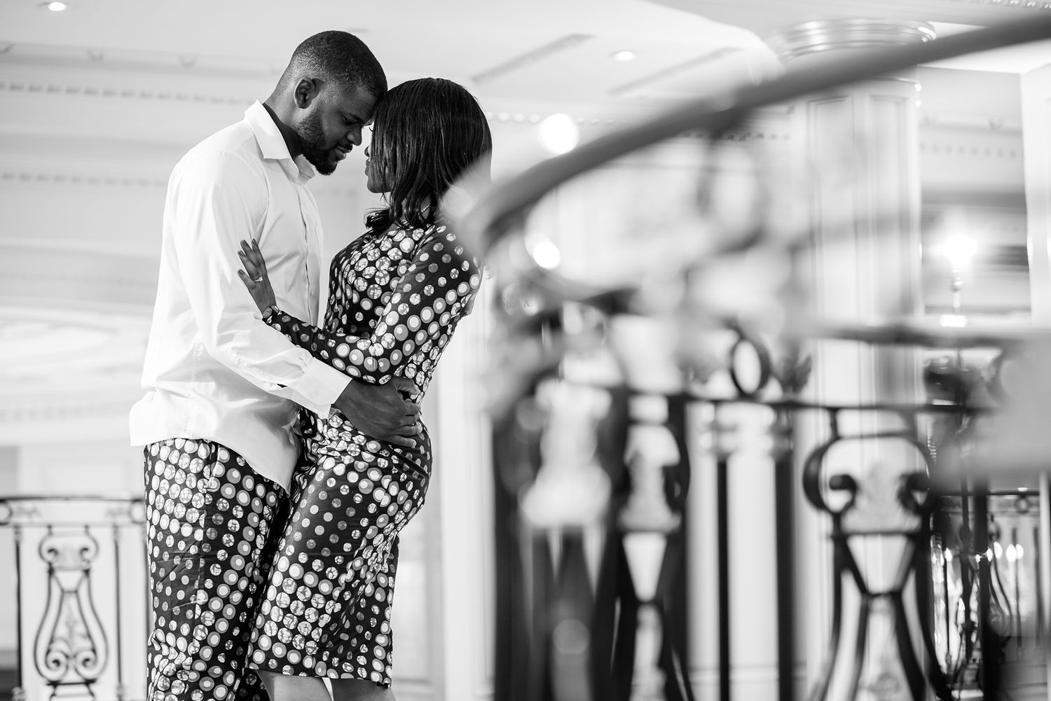 Romantic couple posing along decorative metal railings in an elegant indoor setting.