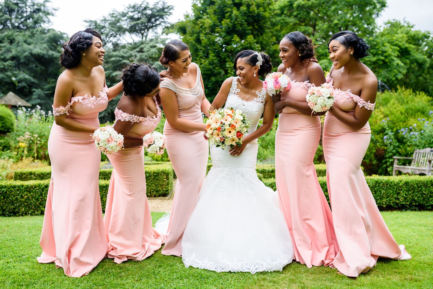 Wedding party in pink bridesmaid dresses posing playfully on green lawn.