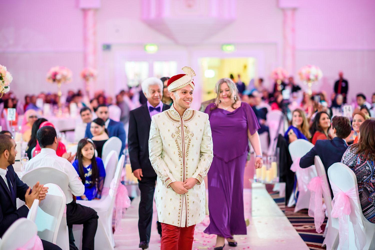 Wedding celebration in grand hall with pink lighting and traditional cultural attire.