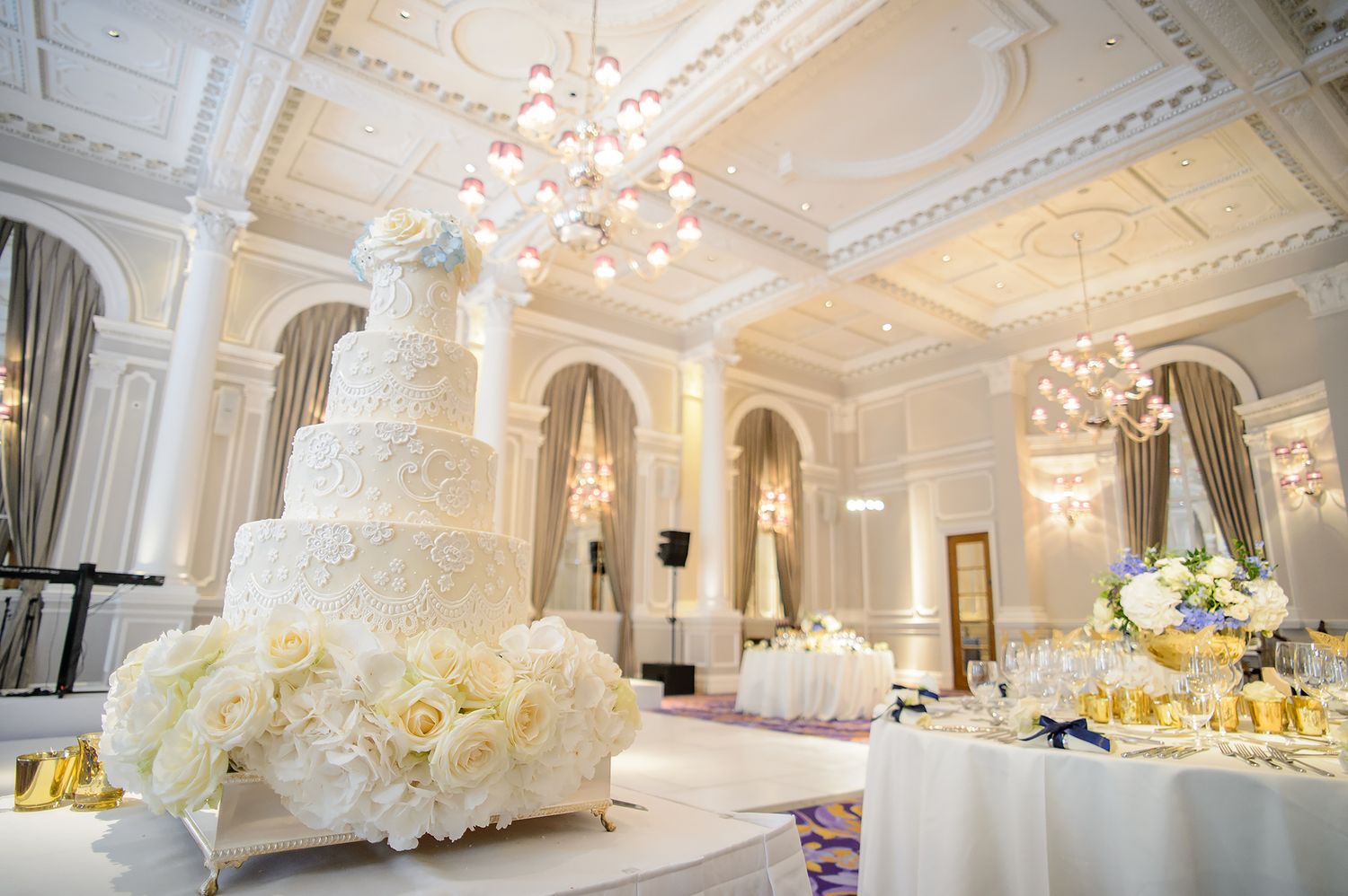 Elegant white wedding cake display in ornate ballroom with crystal chandelier and classical decor.