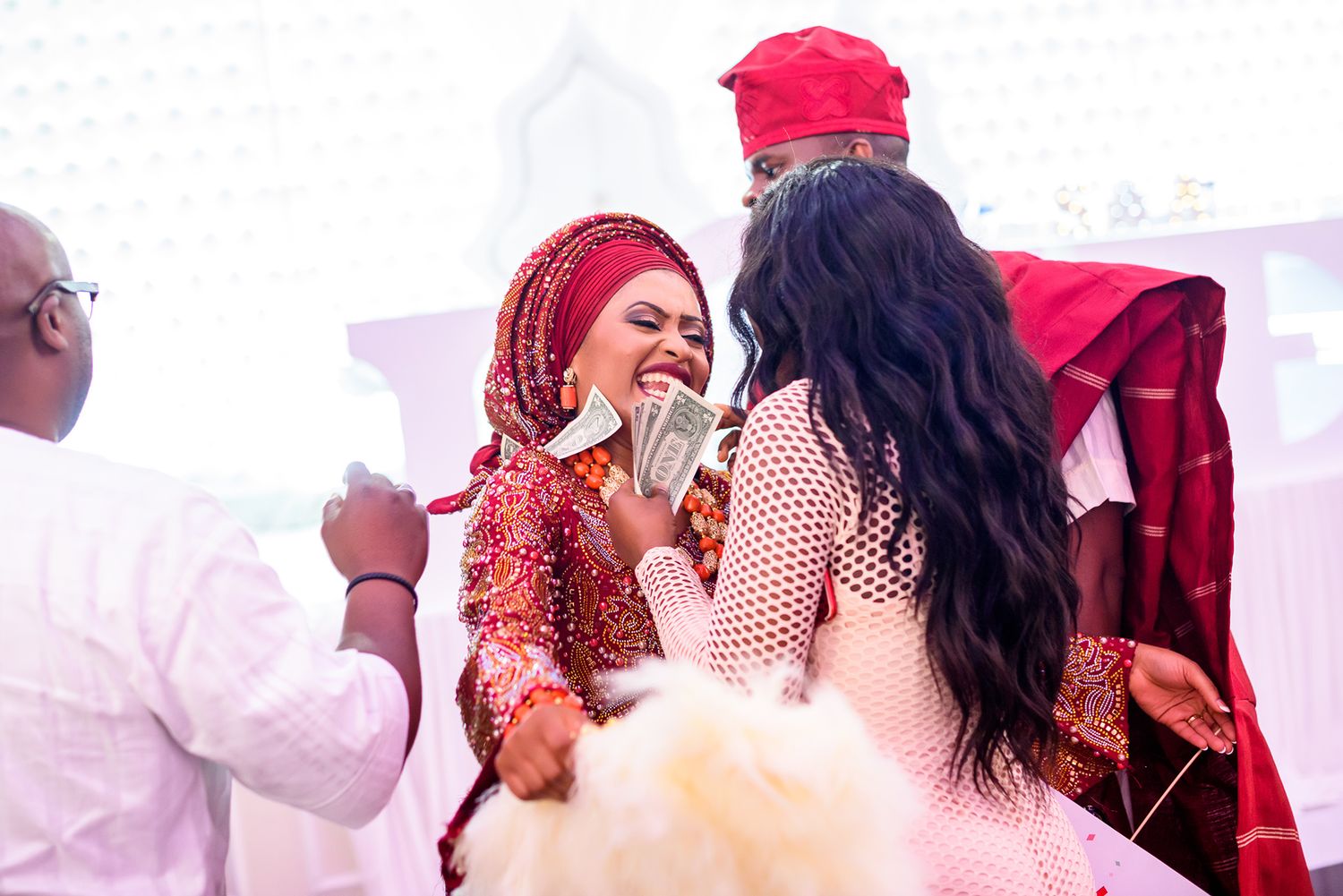 Wedding celebration with guests in red attire dancing under pink ambient lighting.