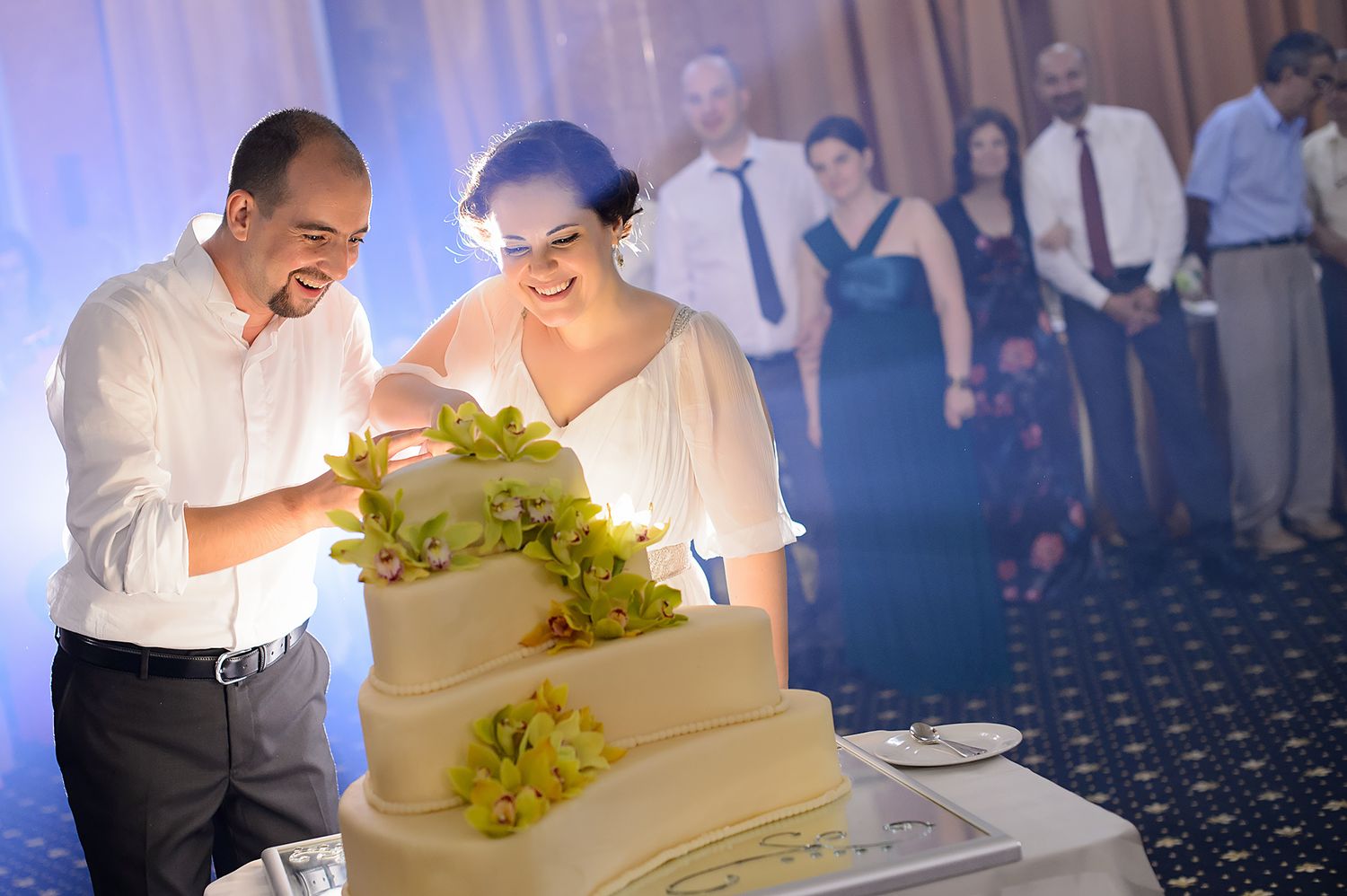 Wedding couple cutting their white tiered cake decorated with green accents.