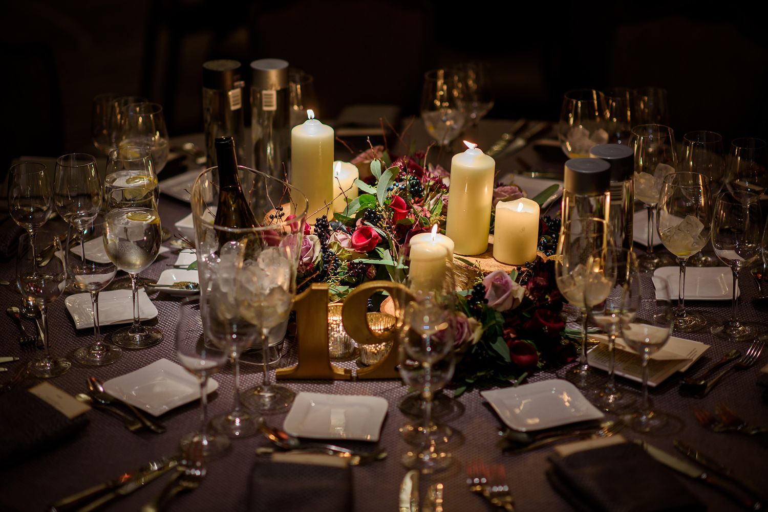 Elegant wedding reception table setting with candles, wine glasses, and floral centerpieces.