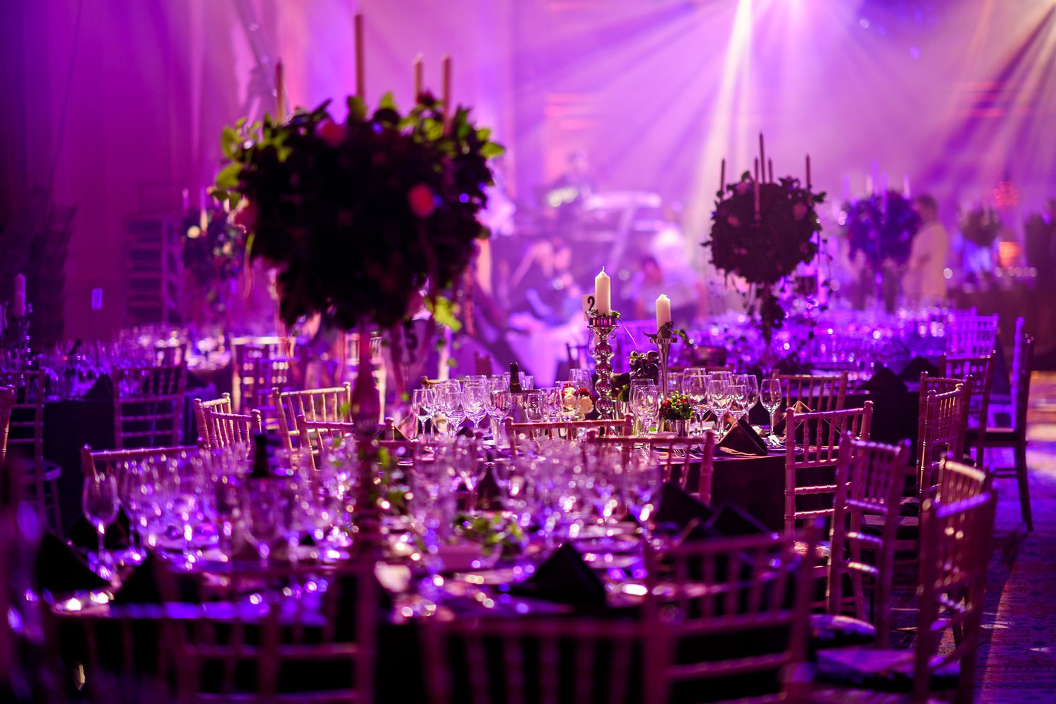 Luxurious wedding reception tables set with elegant centerpieces under dramatic purple lighting.