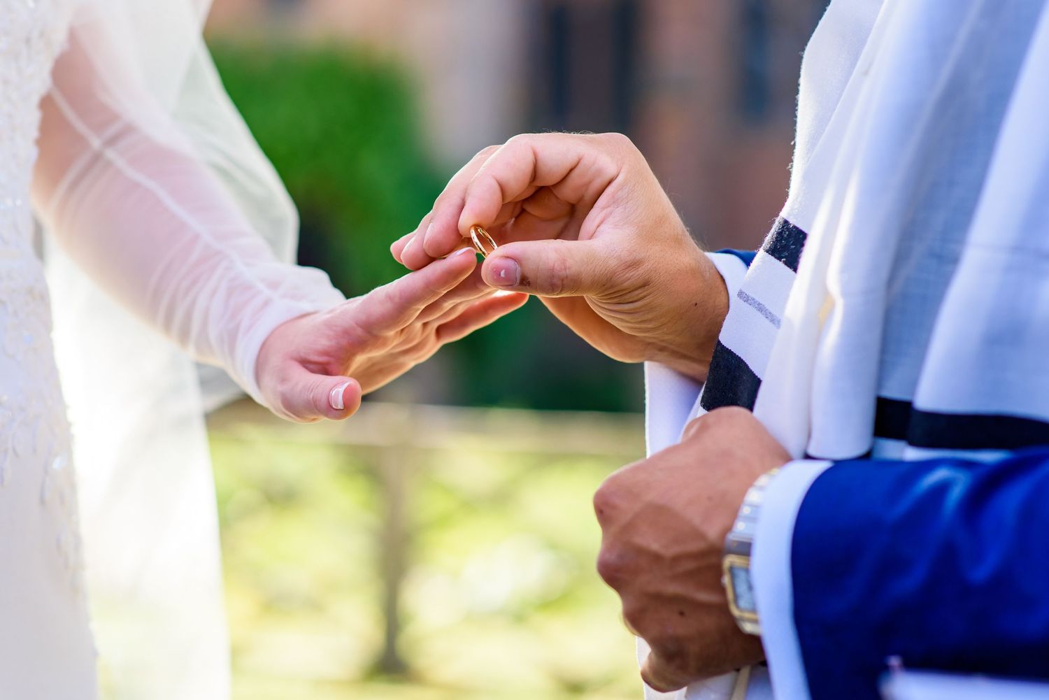 Close-up of hands exchanging rings during outdoor wedding ceremony.