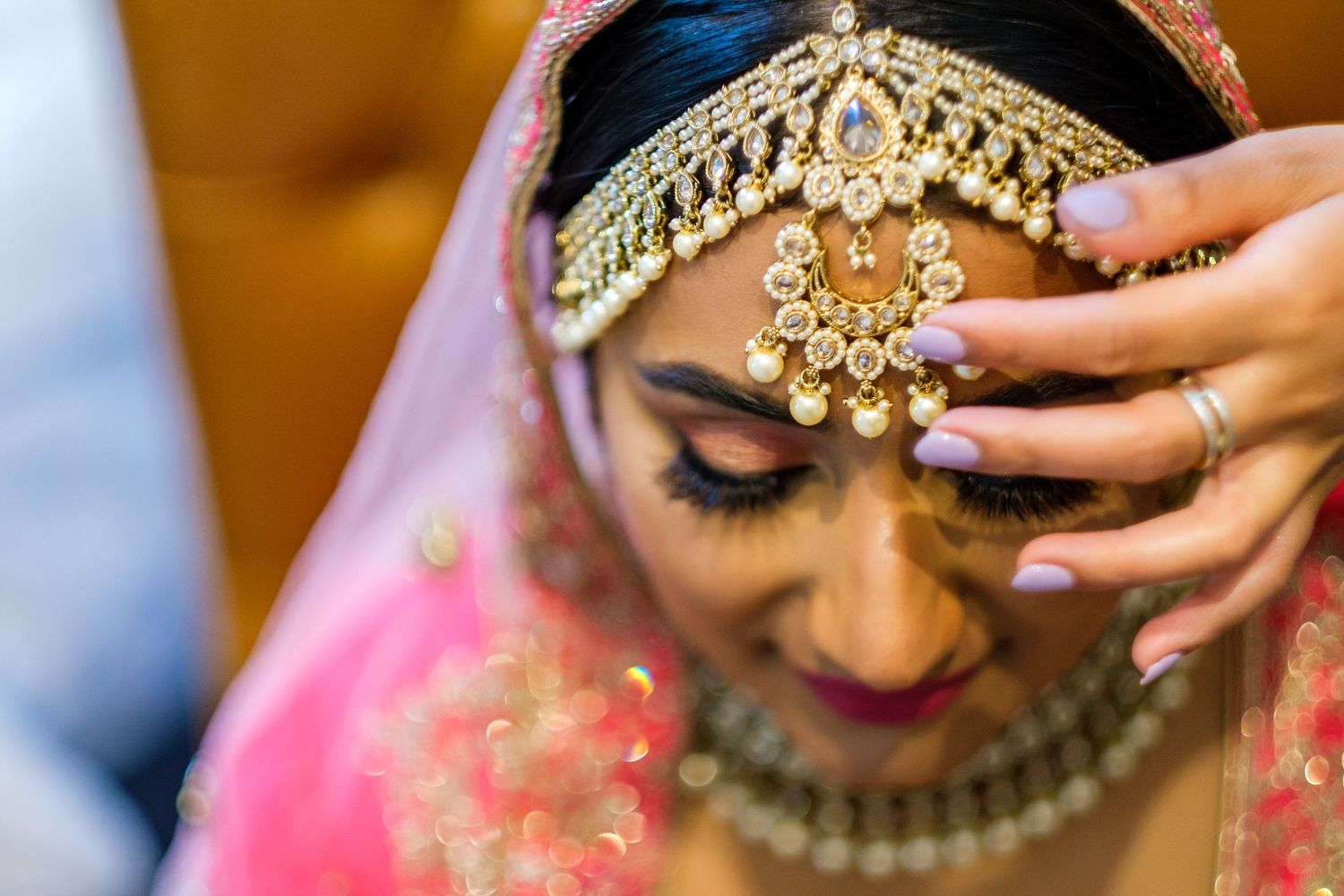 Close-up detail of ornate gold and crystal bridal jewelry and headpiece against warm lighting.