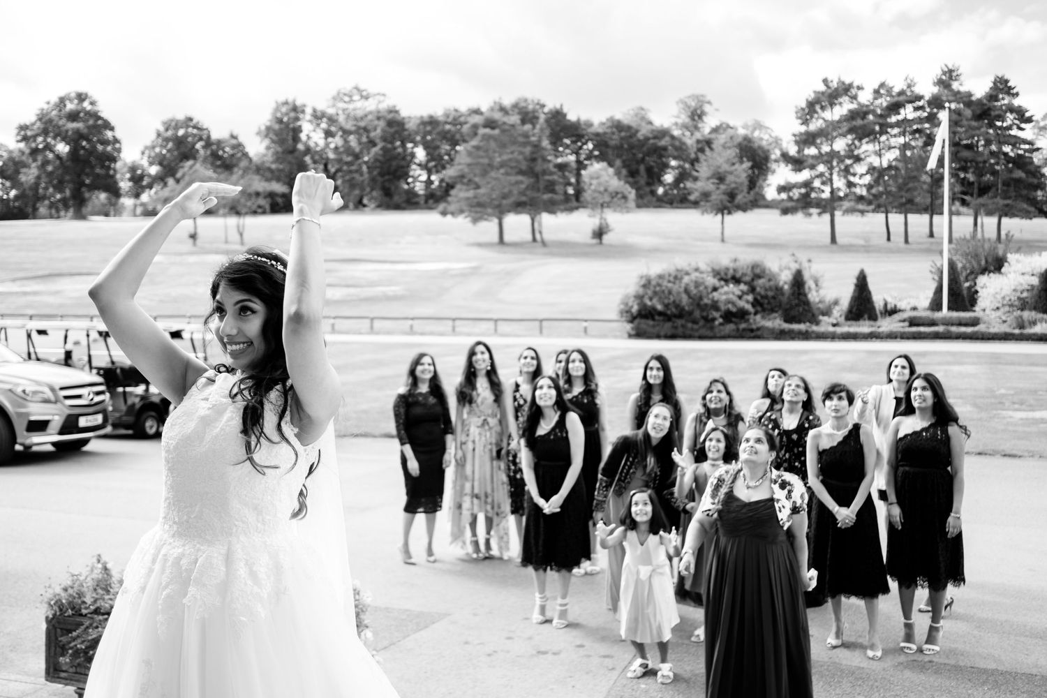Bridesmaids in dark dresses pose outdoors in a line formation.