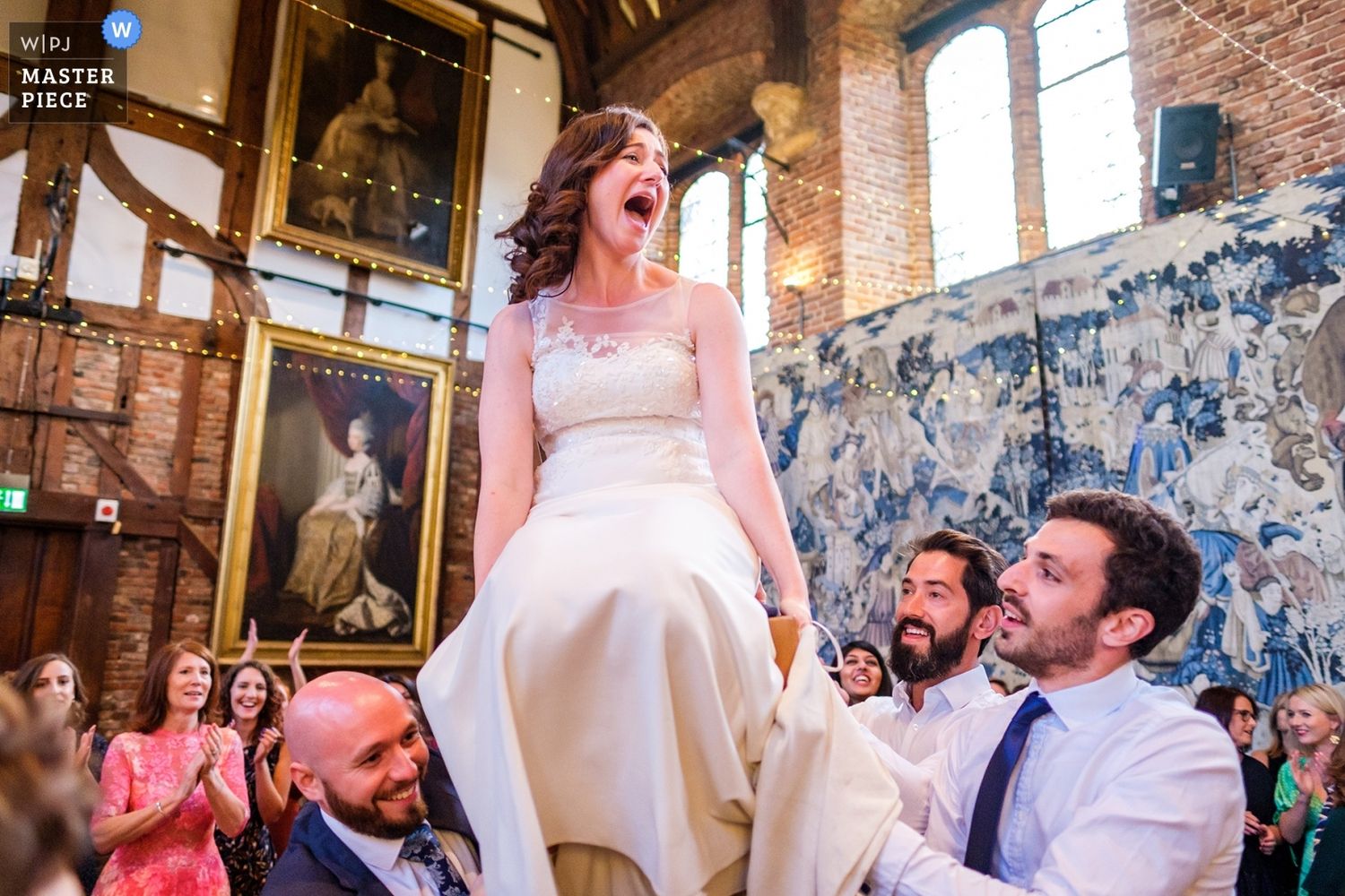 Wedding reception guests dancing and celebrating in a rustic brick venue with string lights.