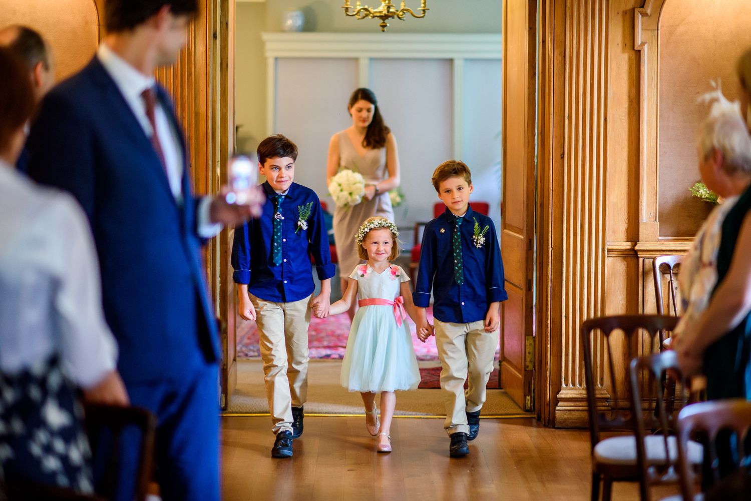 Event guests mingle in an elegant wood-paneled ballroom with chandelier.