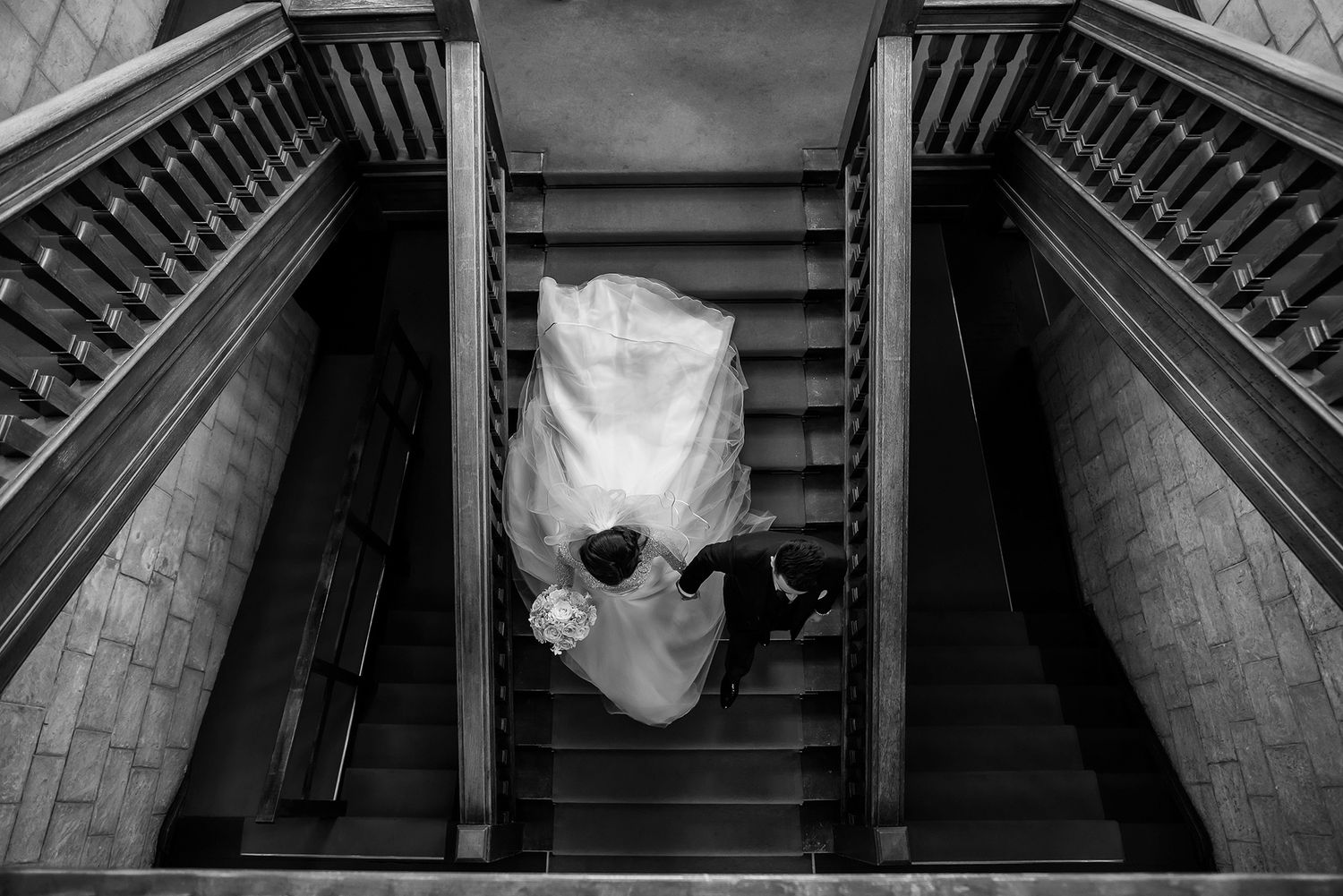 Overhead view of wedding dress flowing down elegant stone staircase in black and white.