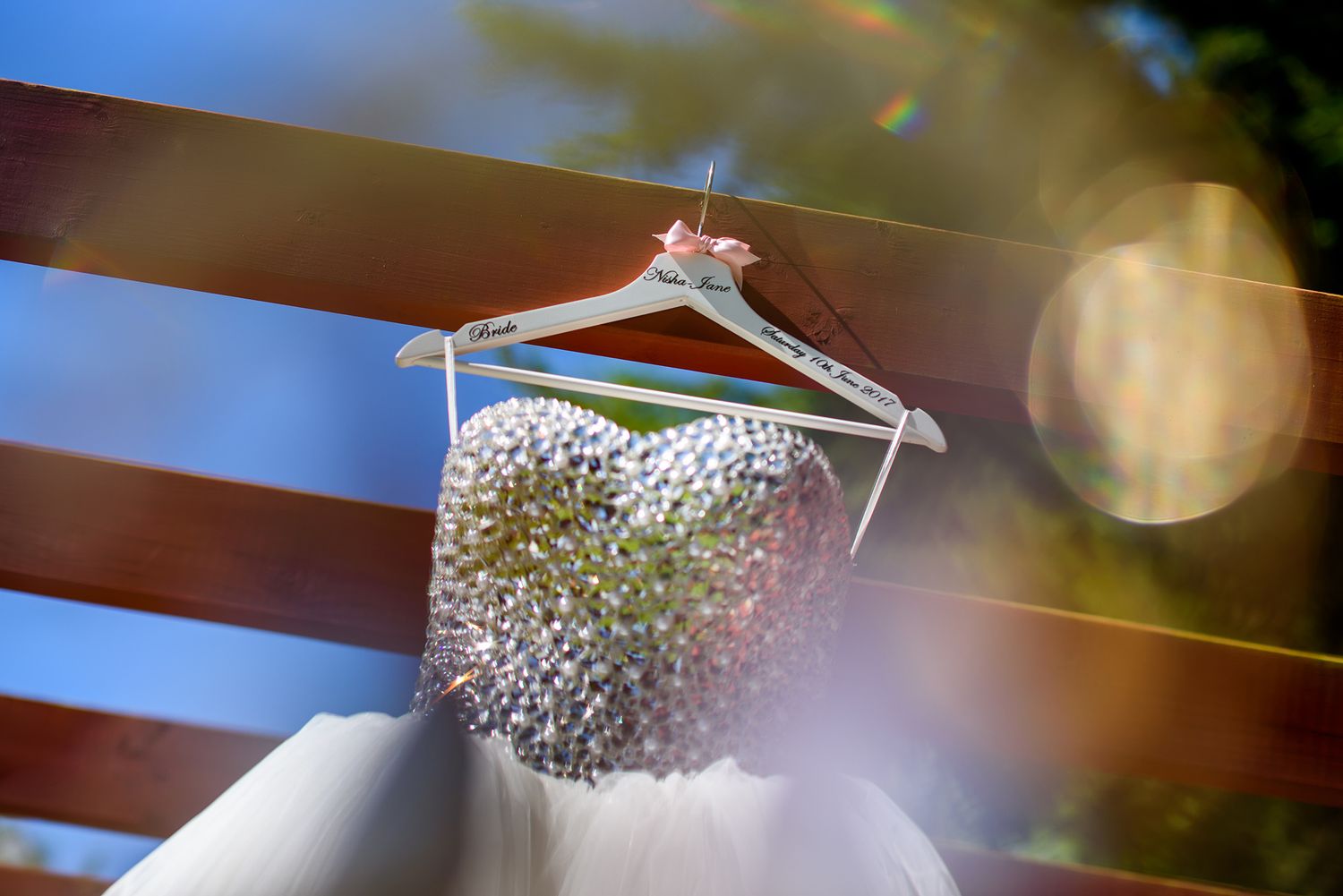 Crystal embellished bridal gown hangs from a wooden beam in natural lighting.