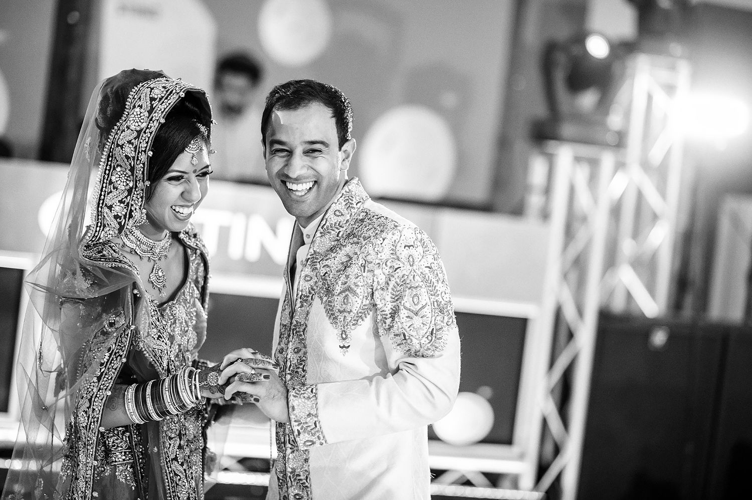 Black and white photo of newlyweds in traditional South Asian wedding attire sharing a joyful moment.