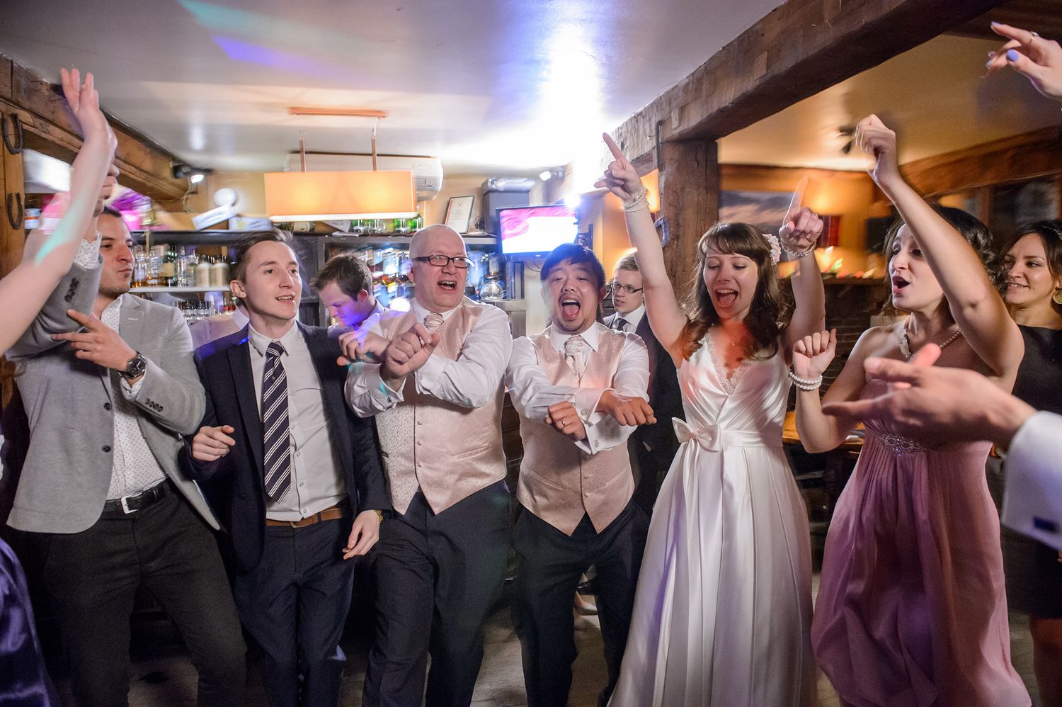 Wedding reception dance floor filled with celebrating guests under bright lights.