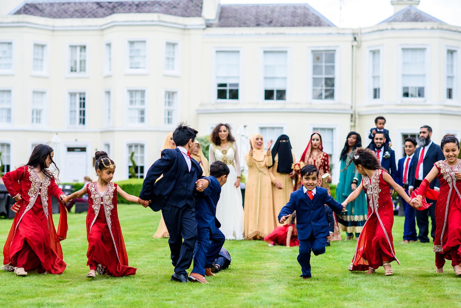 Guests in red and blue attire dancing and celebrating on mansion grounds.
