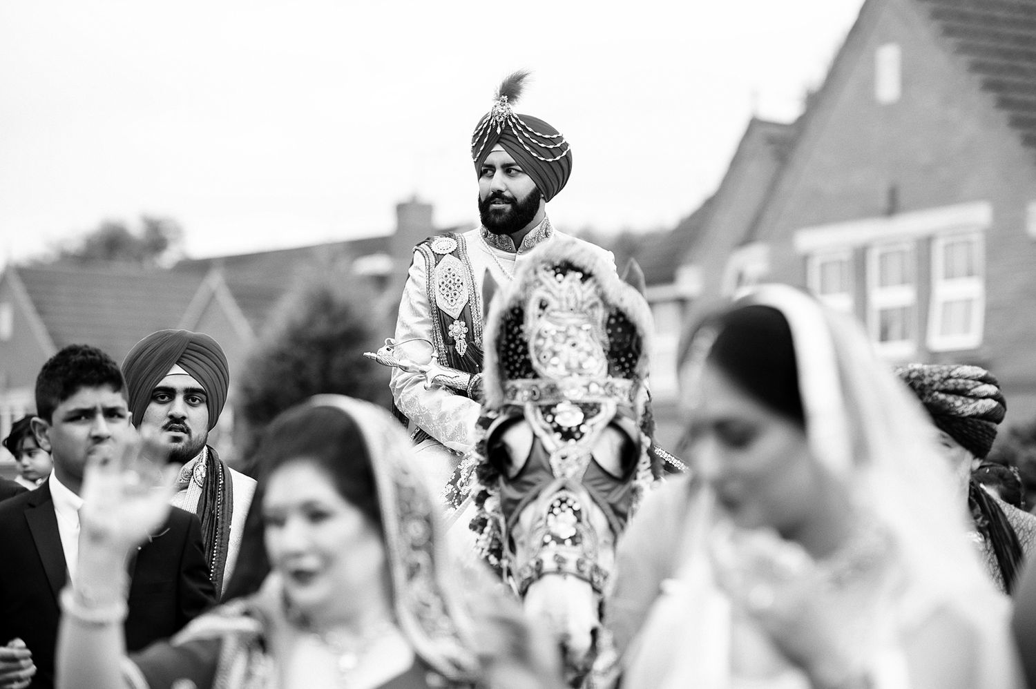 Black and white photograph of a traditional Sikh wedding procession with guests celebrating.