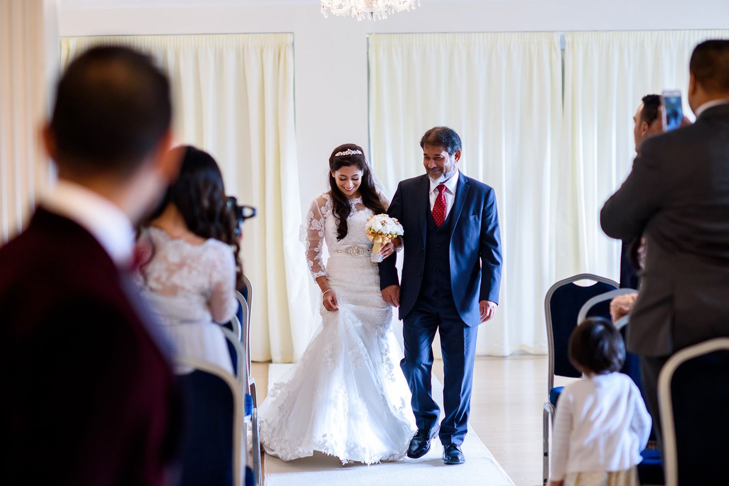 Wedding celebration in an elegant white room with chandelier and flowing curtains.