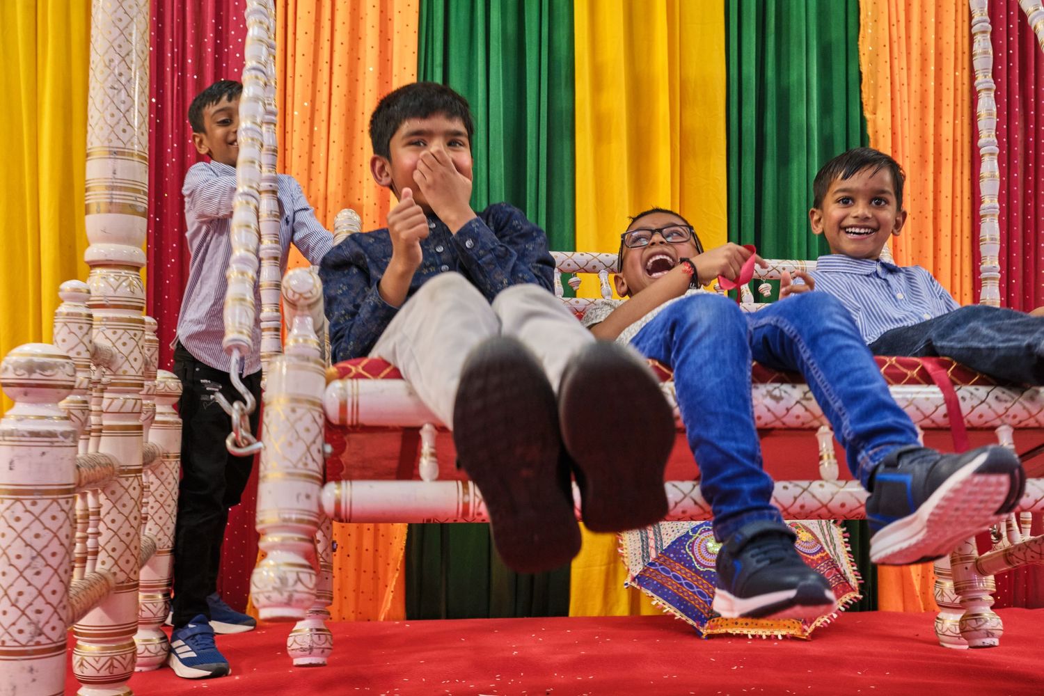 Children laugh and play while lounging on a colorful stage with ornate pillars and vibrant rainbow backdrop curtains.