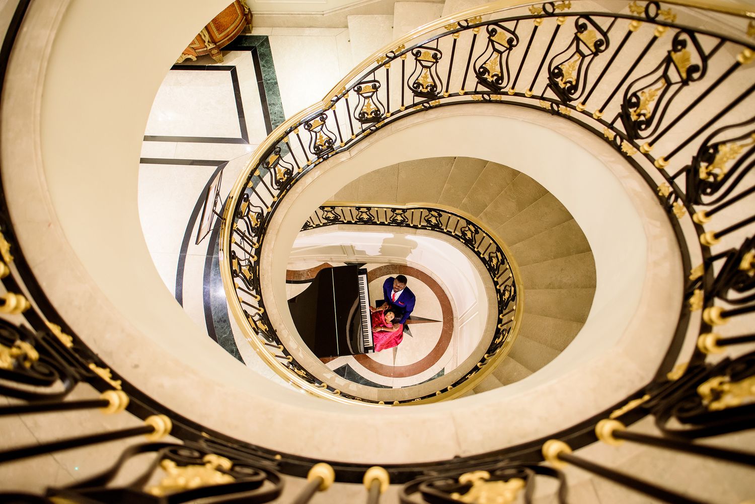 Looking up through a curved spiral staircase with ornate wrought iron railings and cream colored walls.