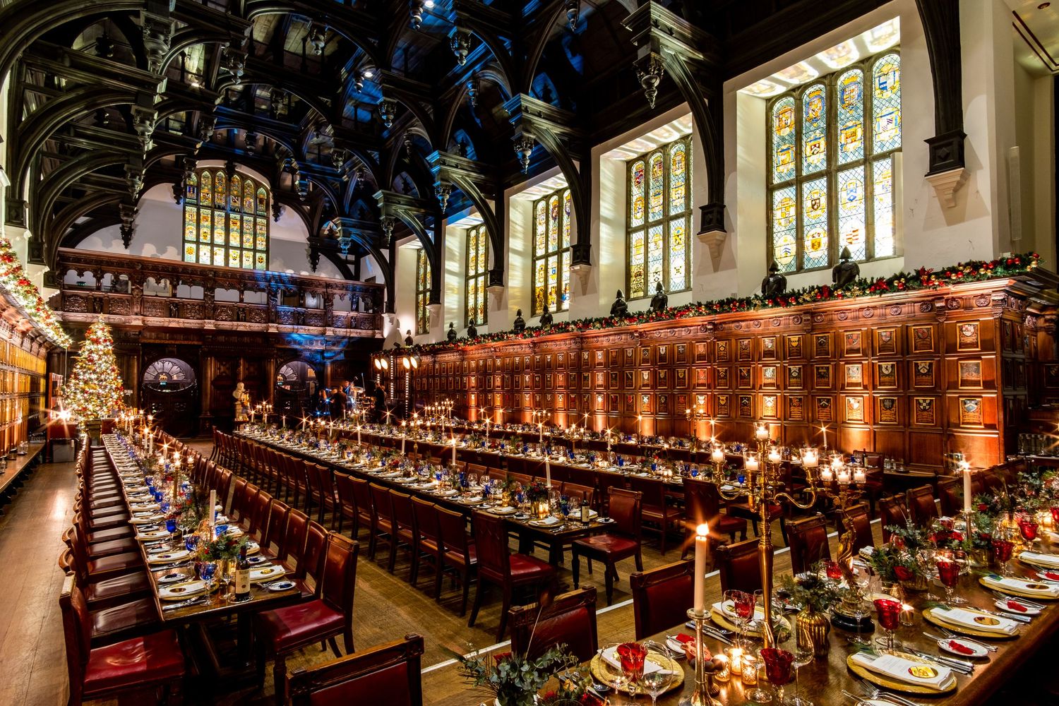 Elegant dining hall with vaulted ceilings and ornate woodwork lit by warm chandelier lighting.