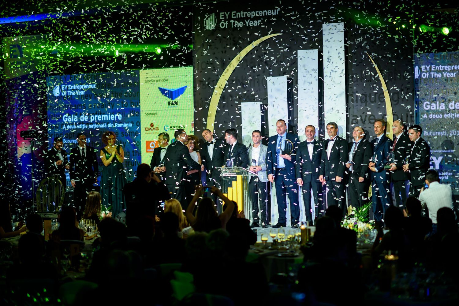 Large audience gathered at a formal awards ceremony with blue and green stage lighting.