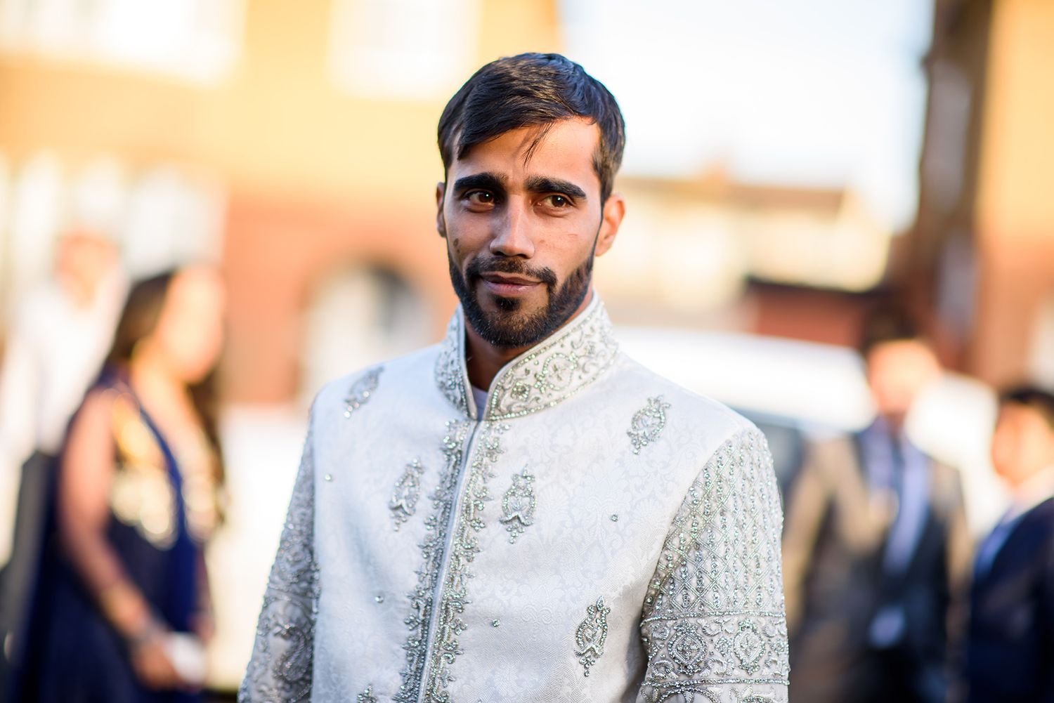 A groom in traditional white embroidered sherwani poses during a wedding celebration.