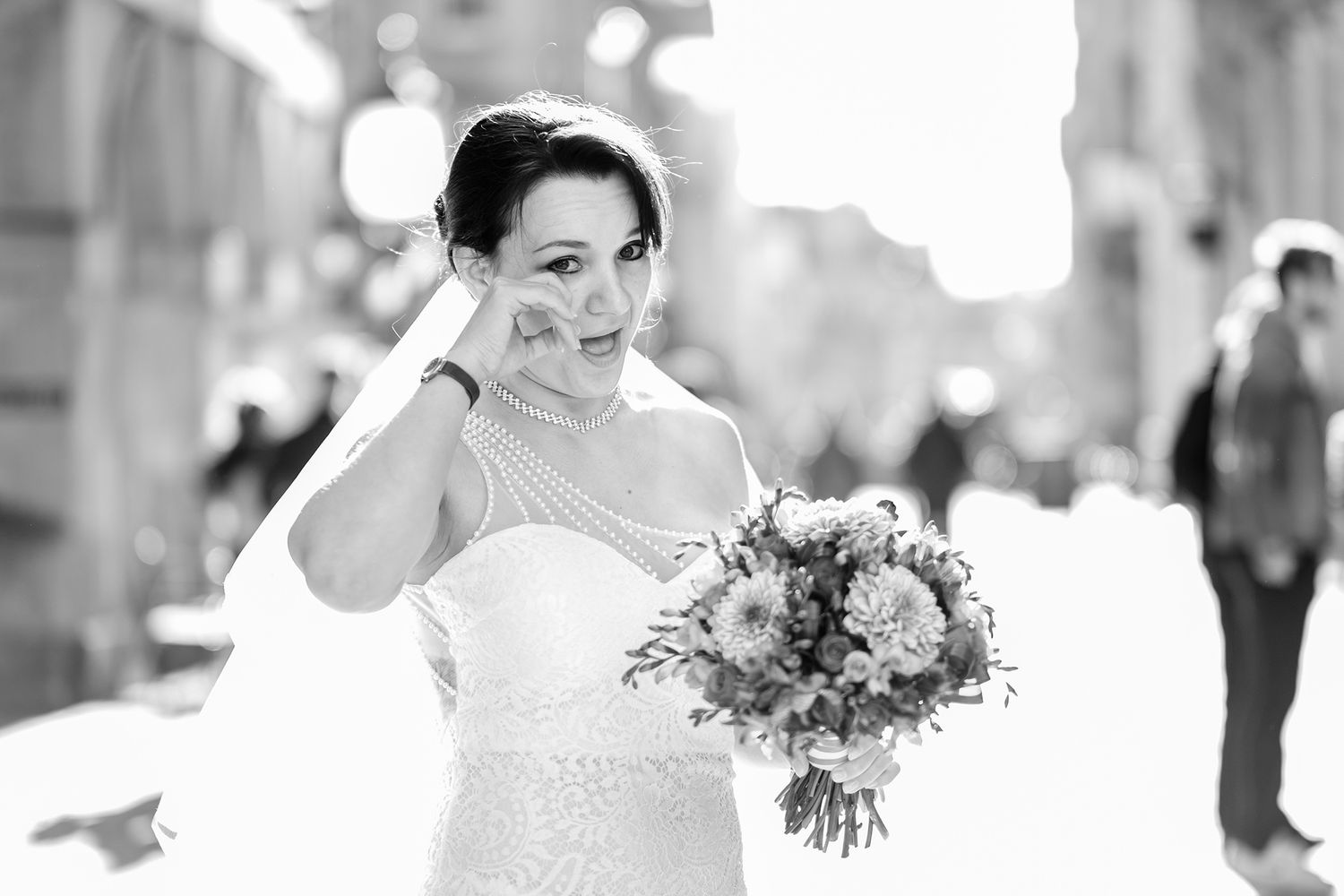 Bride in white dress holding bouquet poses on city street in black and white photography.