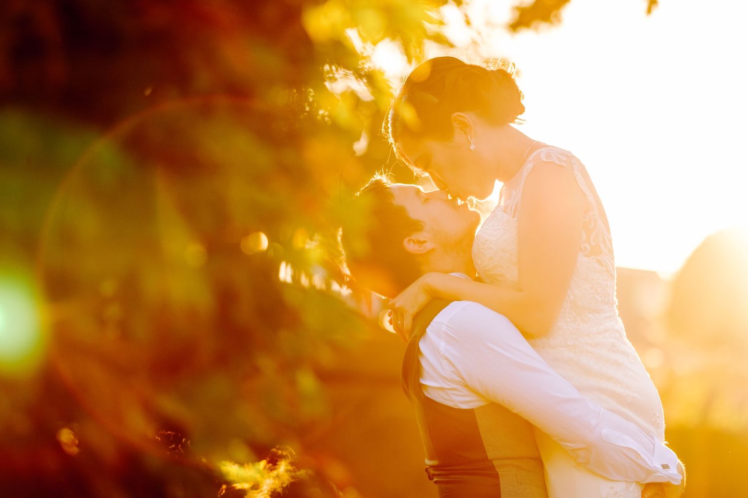 A couple embraces in a golden sunset glow while standing in a lush garden setting.