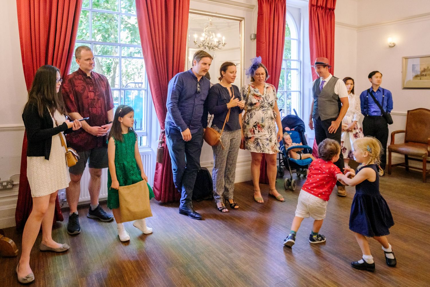 People gathered in a room with red curtains participating in a group dance or activity.
