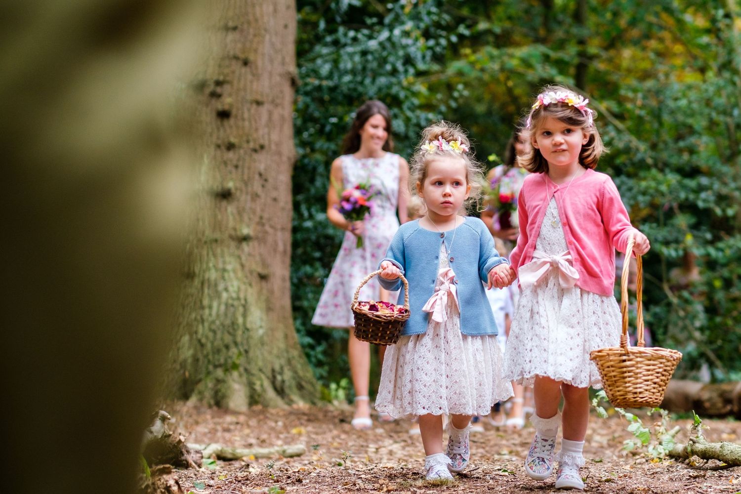 Children walking through a lush forest path carrying baskets and flowers on a sunny day.