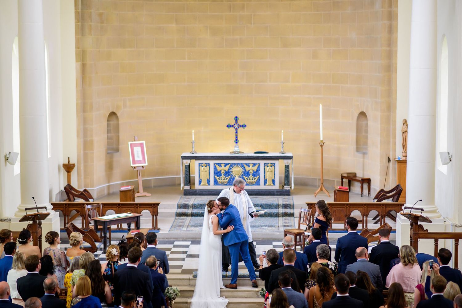 Wide view of a church interior during a ceremony with guests seated in wooden pews.
