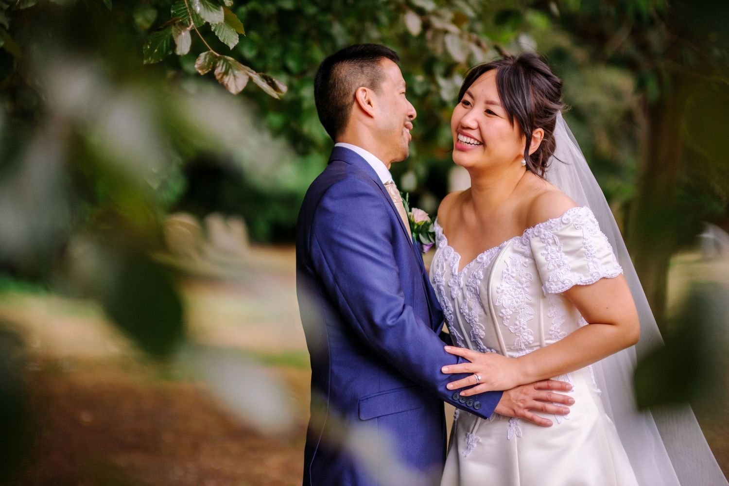 Newlyweds embrace in an outdoor garden setting with lush greenery in the background.