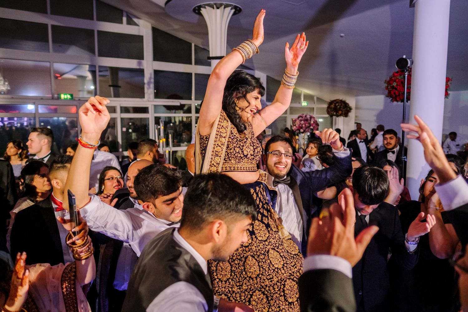 Energetic wedding party dance floor scene with guests dancing under modern venue lighting.