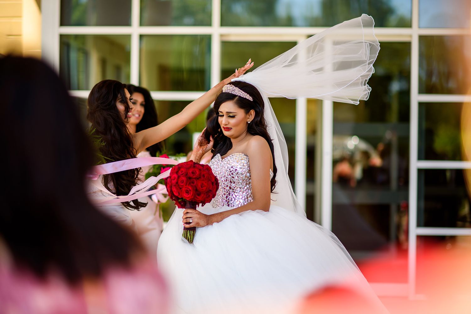 Wedding party poses with flowing white veil against glass building exterior.