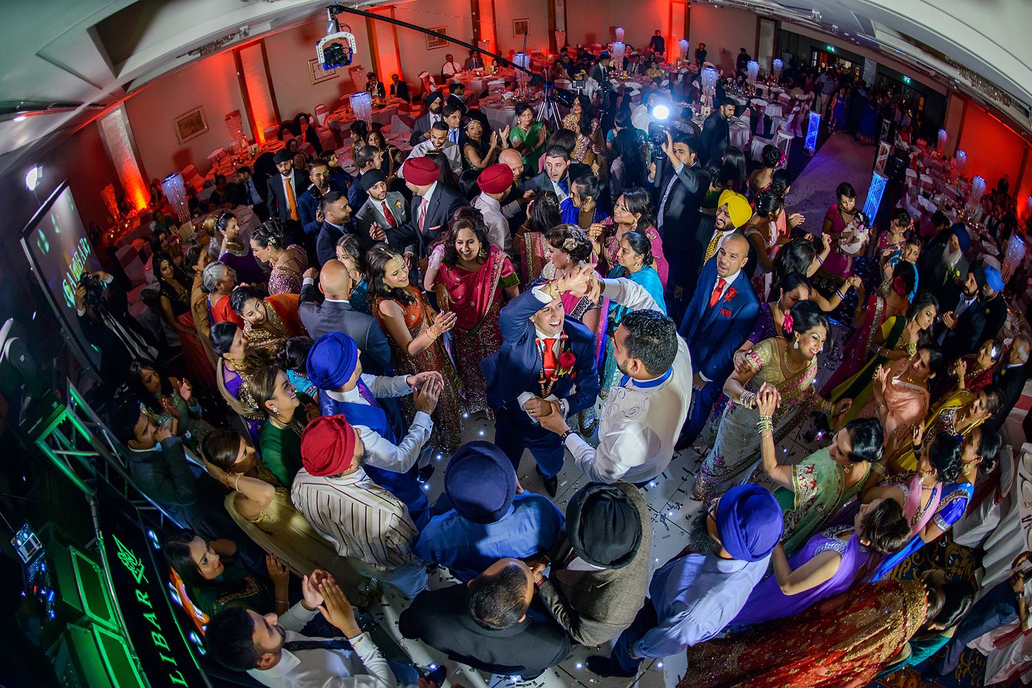 A crowded reception hall illuminated in red and blue lighting during a wedding celebration.