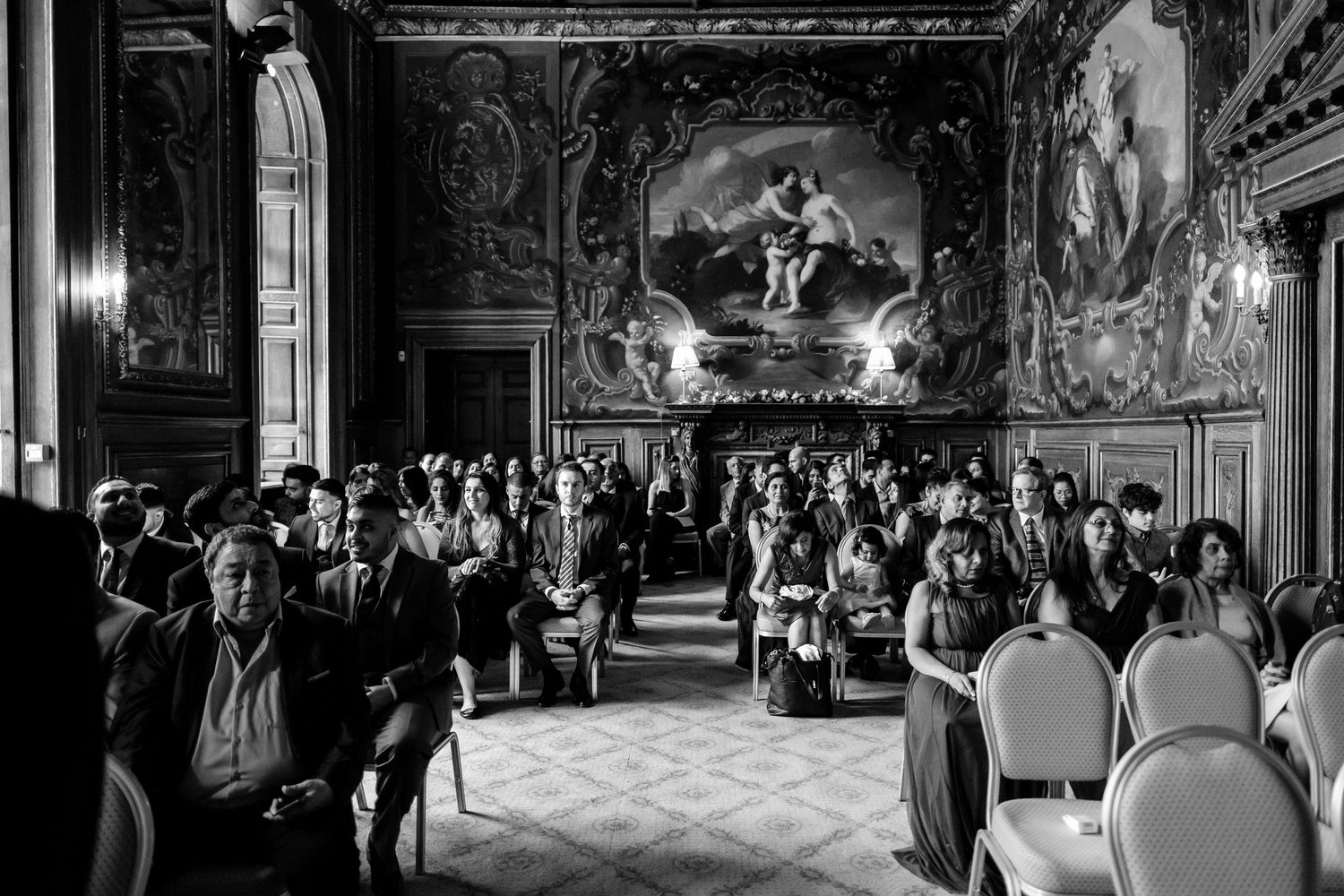 Opulent ballroom wedding venue with grand chandeliers and decorative wall murals.