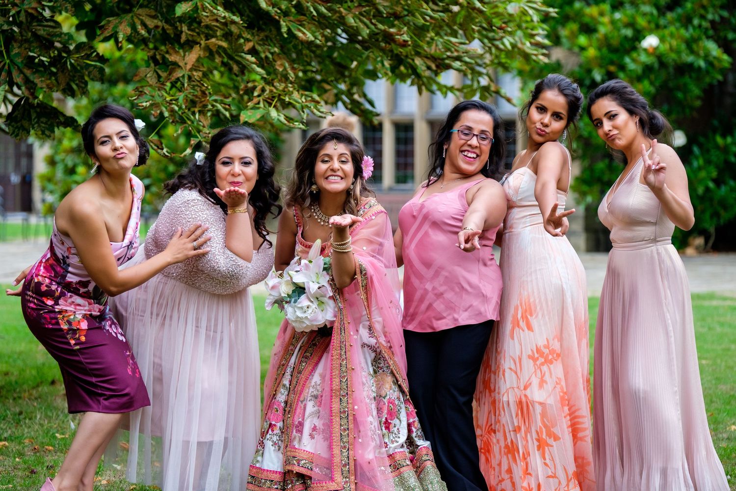 Wedding party in pink and coral dresses posing together in garden setting.